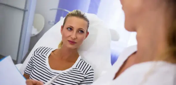 Doctora explicando el tratamiento estético a la paciente recostada en la silla de la clínica